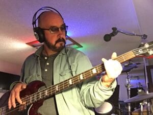 A man with headphones on playing an electric bass.