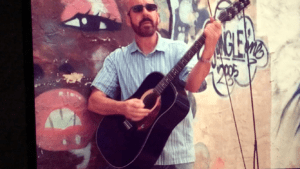 A man holding a guitar in front of a wall.