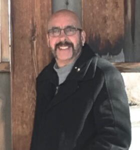 A man with glasses and a beard standing in front of a building.