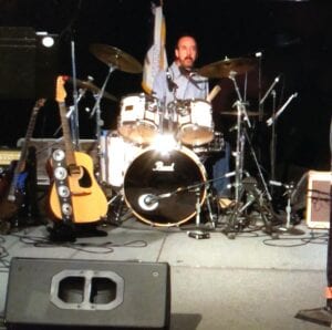 A man playing drums on stage with other instruments.